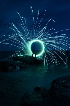 a man standing on top of a rock near the ocean with fireworks in the sky