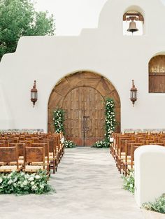 an outdoor wedding ceremony with wooden chairs and greenery on the aisle leading to doors