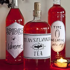 three bottles of spider tea sit on a table with candles in front of the bottles