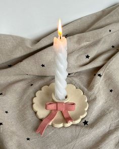 a lit candle sitting on top of a bed next to a pink ribbon and star pillow