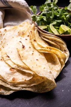 several tortillas are stacked on top of each other with a bowl of cilantro in the background