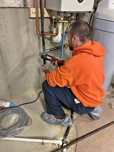 a man is working on a water heater in the basement with hoses attached to it