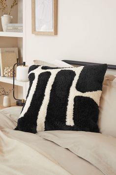 a black and white pillow sitting on top of a bed next to a book shelf