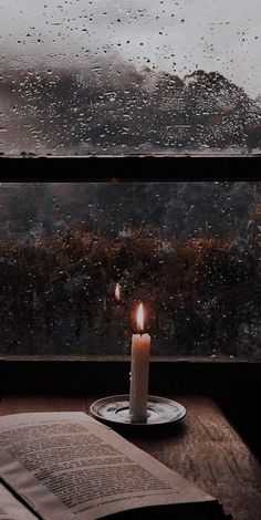 a lit candle sitting on top of a table next to an open book and window