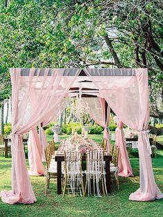 an outdoor wedding setup with pink drapes and white tablecloths on the grass