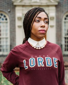 a woman with dreadlocks standing in front of a brick building wearing a maroon sweatshirt