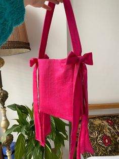 a person holding a pink bag on top of a table next to a lamp and potted plant