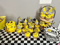 a table topped with cupcakes covered in yellow and black frosting next to a cake