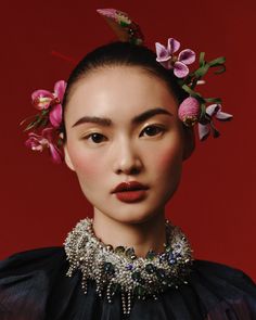 a woman with flowers in her hair wearing a black dress and statement necklace, against a red background