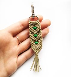 a hand holding a keychain with green beads and tassels on it