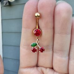 a person is holding a gold colored belly ring with red, green and pink stones