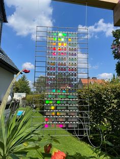 a sculpture made out of many different colored objects in front of some bushes and trees