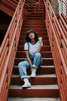 a woman sitting on some stairs with her hand in her pocket and looking up at the camera