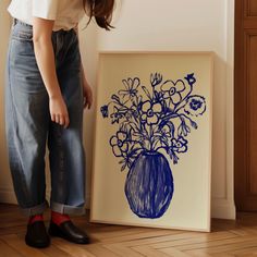 a woman standing next to a blue vase with flowers in it on a wooden floor