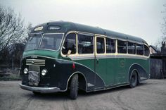 an old green bus parked in a parking lot next to a fence and tree with no leaves on it