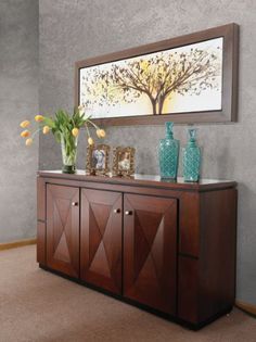 a wooden sideboard with vases and flowers on it in front of a painting