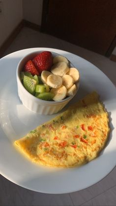 an omelet on a plate next to a bowl of sliced bananas and strawberries