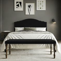 a bed with white sheets and black headboard sitting next to two pictures on the wall