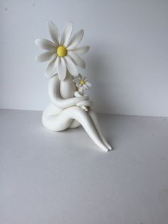 a white ceramic figurine with a flower in its lap sitting on a table