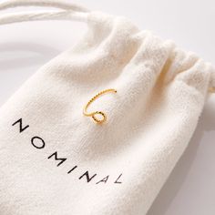 a small gold ring sitting on top of a white drawstring bag that says nominal