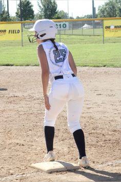 a female baseball player standing in the outfield with her helmet on and knee up