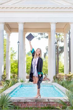 a woman holding up her graduation cap in front of a pool with columns and pillars