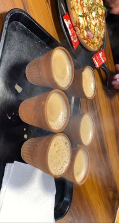 four glasses of beer sitting on top of a table next to a tray with pizza