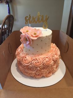 a three tiered cake decorated with pink roses and gold glitters sits in a cardboard box