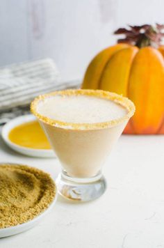 a white table topped with two glasses filled with liquid and pumpkins in the background