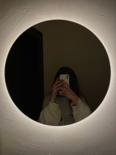 a woman taking a selfie with her cell phone in front of a circular mirror