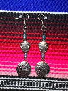 "These handmade sea theme earrings are adorned with silver plated metal shells along with blue semi-precious beads. The ear wire is metal and hypo allergenic.  The matching boot bracelets are available for sale as well. Earrings are 3 1/2\" long. Please see the photos for other earring styles. Price includes one pair of Sand Dollar Silver Shell Earrings with Crystals and Blue Beads. Not water-resistant. For pierced ears only." Beach Beaded Metal Earrings, Metal Beaded Earrings For Beach, Adjustable Metal Earrings For Beach, Handmade Metal Beaded Earrings For Beach, Blue Festival Jewelry Ocean-inspired, Blue Ocean-inspired Jewelry For Festivals, Blue Ocean-inspired Festival Jewelry, Blue Metal Jewelry For Beach, Nickel-free Silver Ocean-inspired Earrings