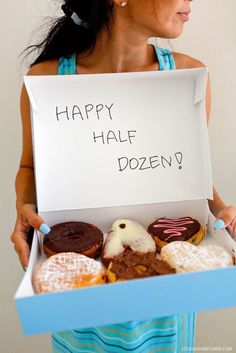 a woman holding a sign that says happy half dozen donuts in front of her face