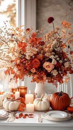 an arrangement of flowers, candles and pumpkins is displayed on a dining room table