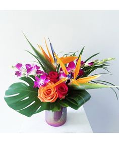 a vase filled with lots of colorful flowers on top of a white table next to a wall