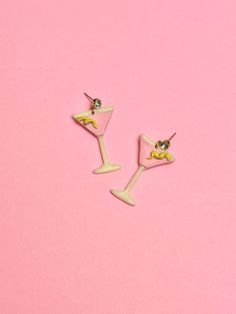 two small yellow and white wine glasses on a pink background, one with a green nose ring