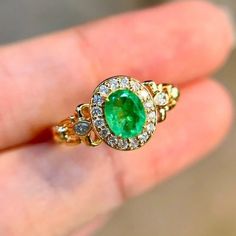 a close up of a person's hand holding a ring with an emerald and diamonds on it