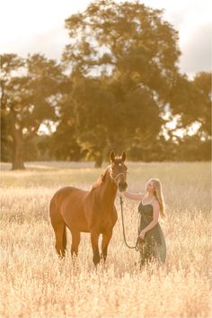 a woman is petting a brown horse in a field with tall grass and trees