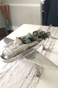 a silver model airplane with succulents in it sitting on a white table