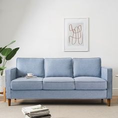 a blue couch sitting in a living room next to a white table and potted plant