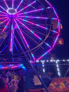 a ferris wheel lit up at night with people standing around it and lights in the background