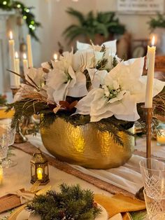 a table set for christmas with candles and flowers in a gold bowl on the centerpiece