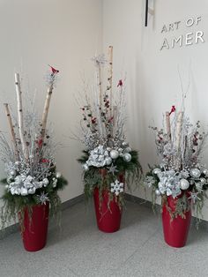 three red vases with white flowers and branches in them are sitting on the floor