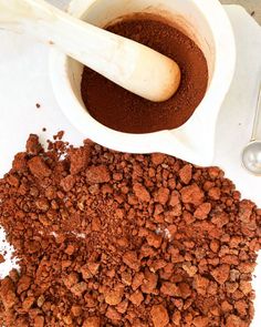 a bowl filled with chocolate next to a scoop of cocoa on top of a table