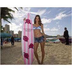 a beautiful woman holding a pink surfboard on top of a sandy beach next to the ocean