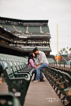 a man and woman kissing on the bench at a baseball stadium with empty seats in front of them