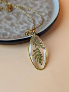 a necklace with a green leaf design on it sitting next to a plate that has a gold chain