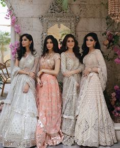 four women in dresses standing next to each other near a wall with flowers on it