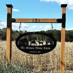 the brown horse farm sign is in front of a field with tall grass and trees