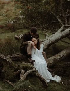 a man and woman sitting on top of a tree branch in the grass with their arms around each other