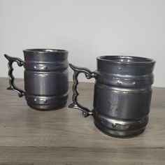 two metal mugs sitting next to each other on top of a wooden table,